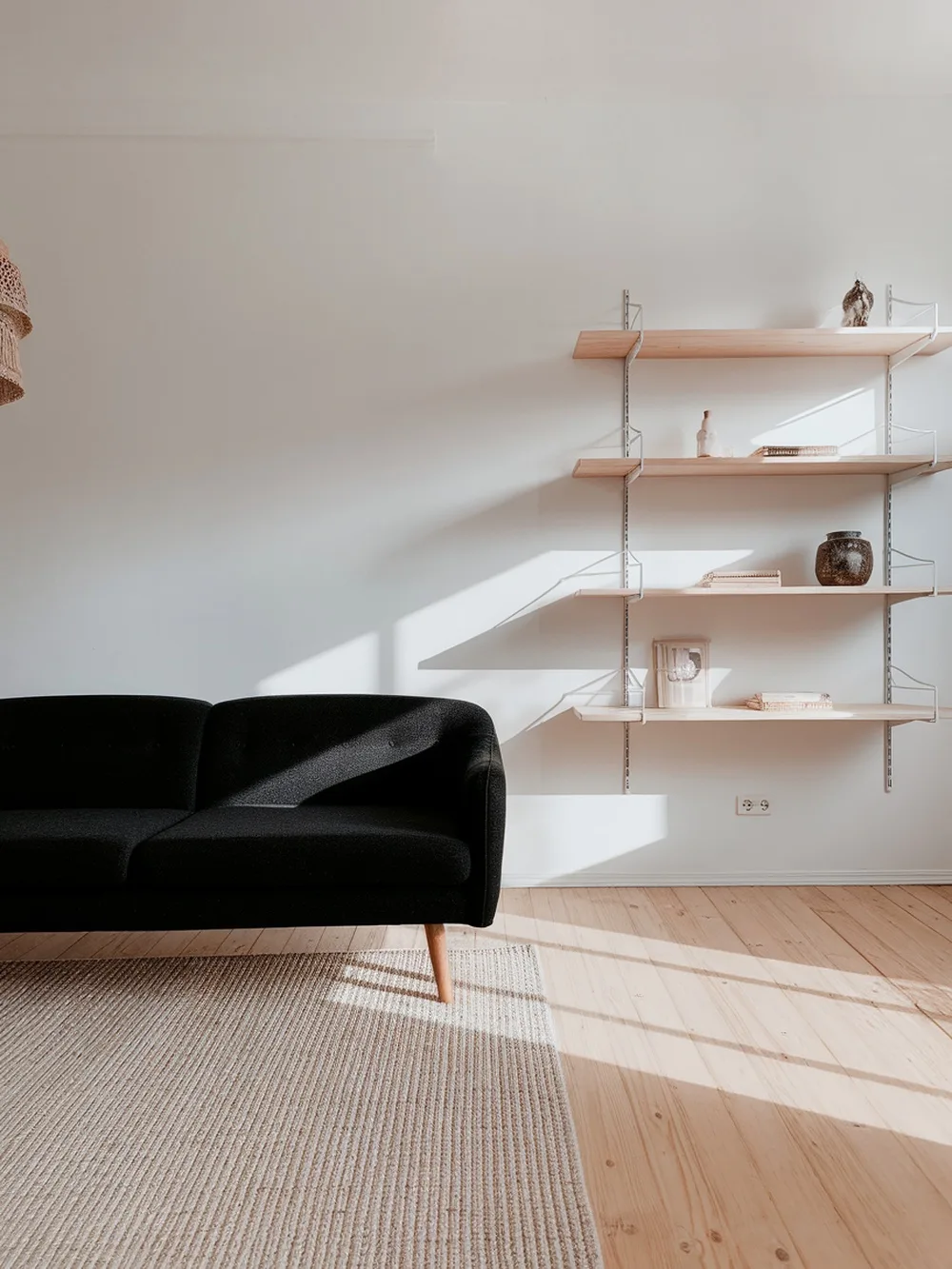 A black couch in a Scandinavian-style living room with natural wood shelves and flooring.